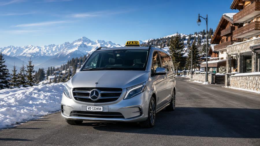 Taxi Mercedes Classe V argentée sur la route d'une station de ski au soleil, chalets et sommets — transfert ski porte à porte