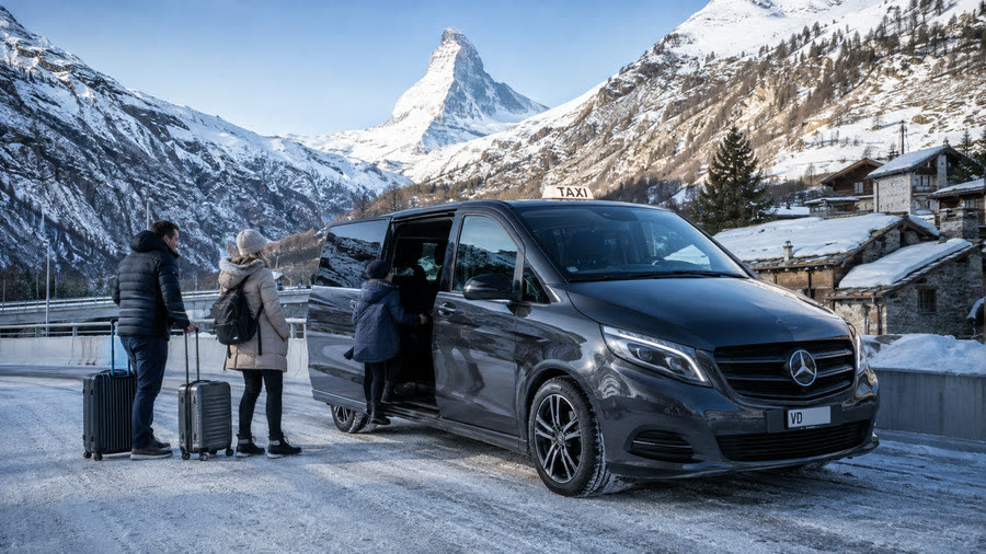 Famille avec valises montant dans un taxi Mercedes Classe V face au Cervin, Zermatt — transfert ski en famille depuis Lausanne